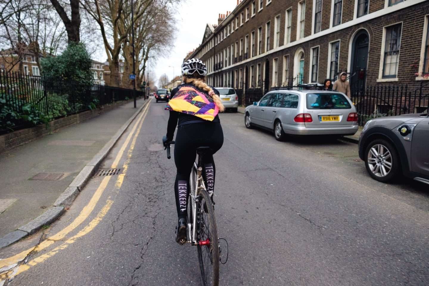 woman cycles London streetpath with Wizard Works Scraptacular Musette on her back in centre of photo
